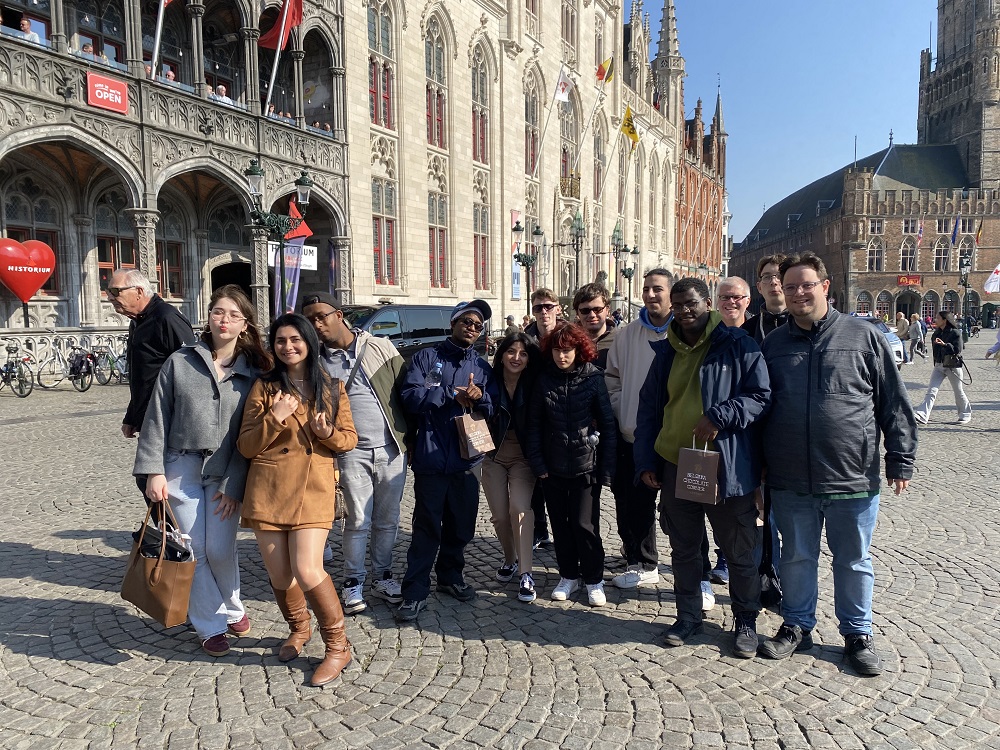 Das Bild zeigt eine Gruppe junger Erwachsener, die auf einem Platz vor Gebäuden in der Stadt Antwerpen steht.